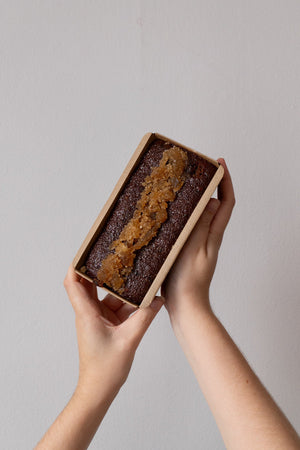 hands holding a rectangular cake with crystallised ginger topping on a grey background.